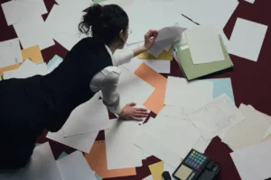 Mujer trabajando en suelo sobre varios documentos dispersos y desordenados